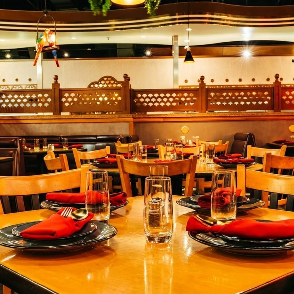 Warmly lit restaurant dining room with wooden tables, black plates, red napkins, leather booths, and ornate carved partitions.