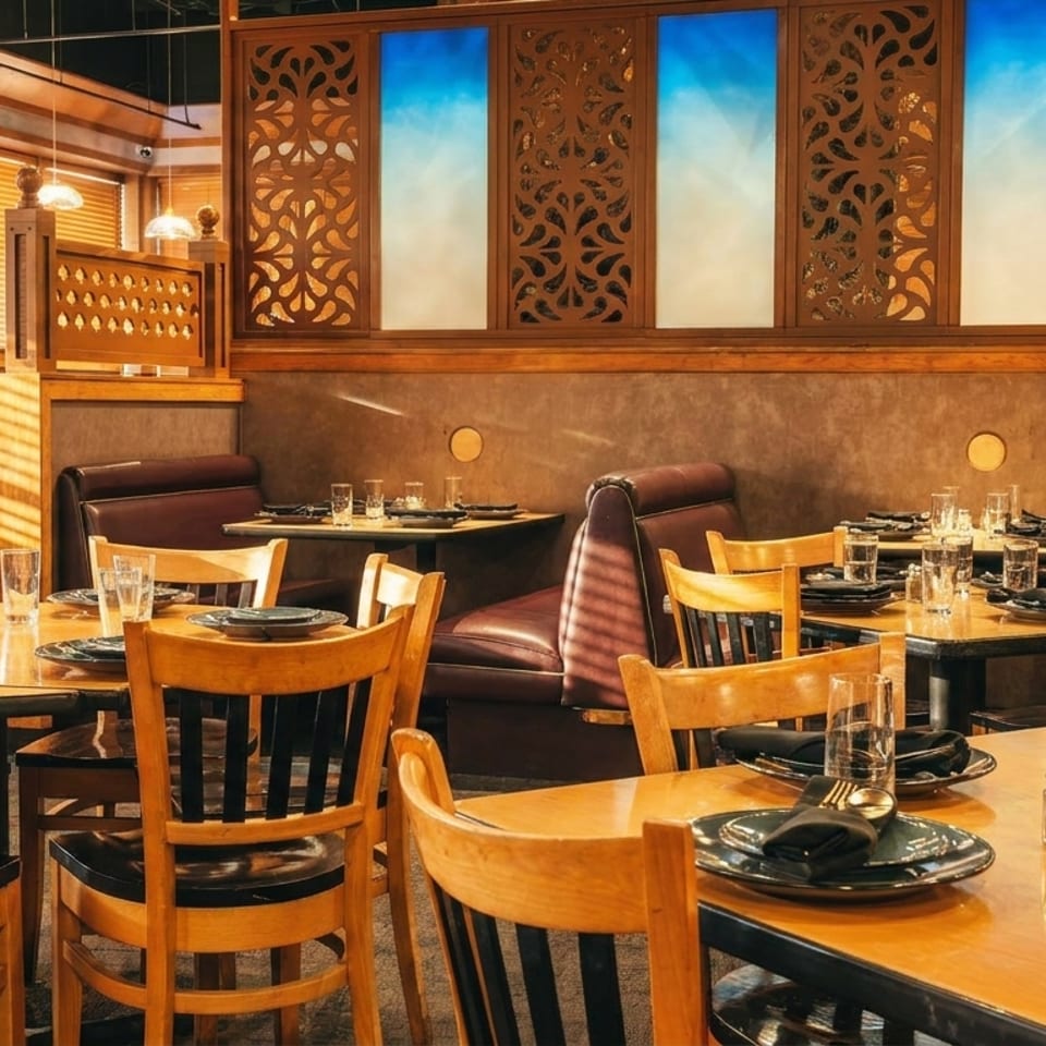 Warmly lit restaurant dining room with wooden tables, black plates, glassware, leather booths, and ornate carved screens.