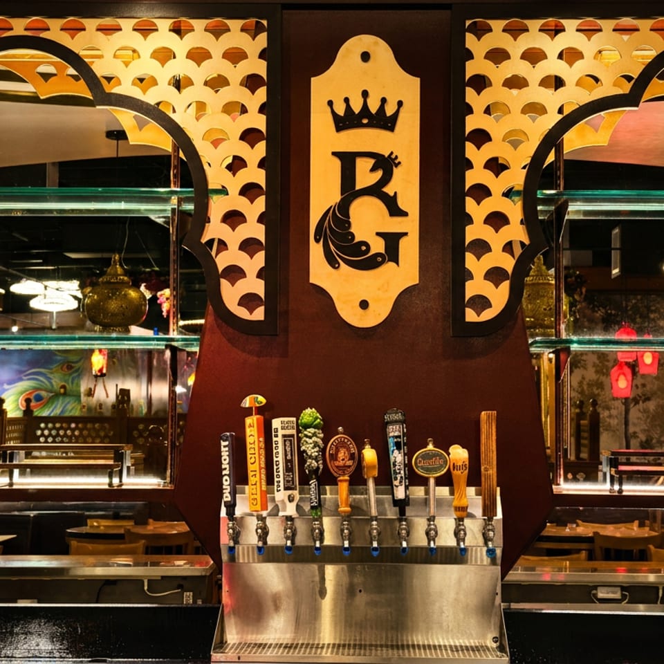 Ornately decorated restaurant bar featuring multiple beer taps, mirrored shelving, pendant lights, and a crowned logo.