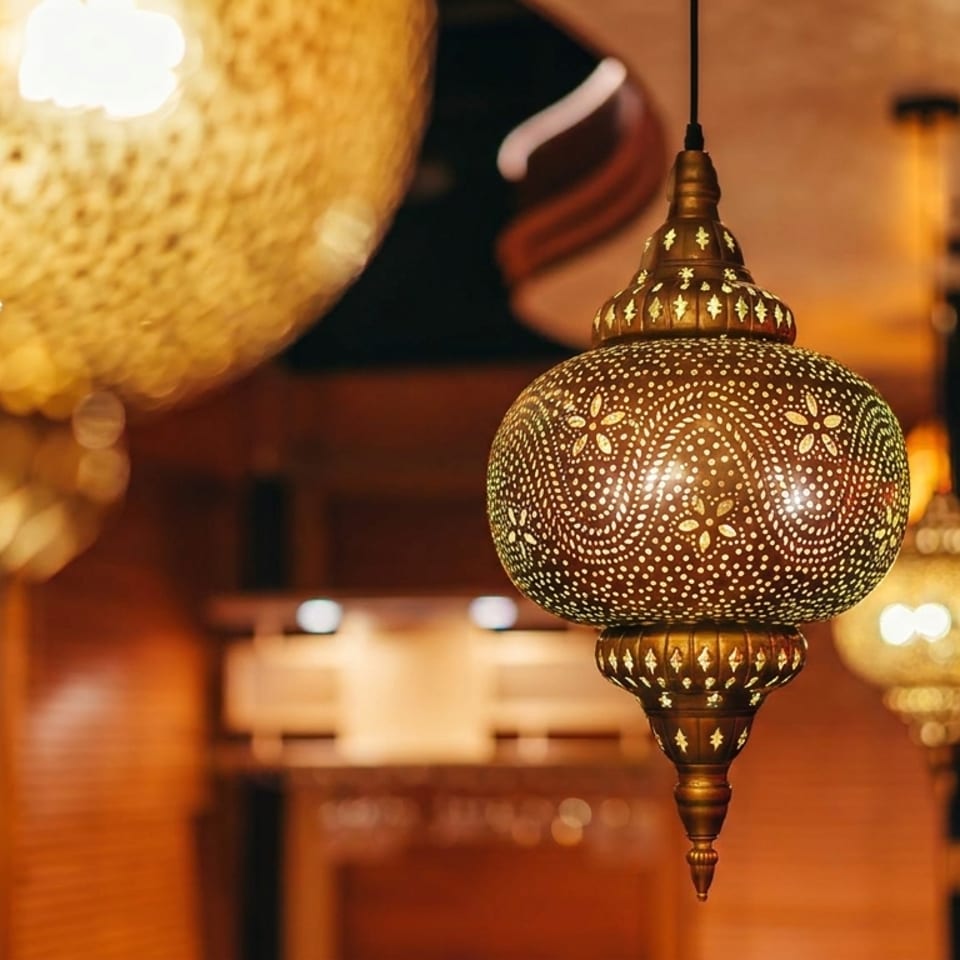 Ornate Moroccan pendant lanterns glow warmly inside a richly decorated restaurant.
