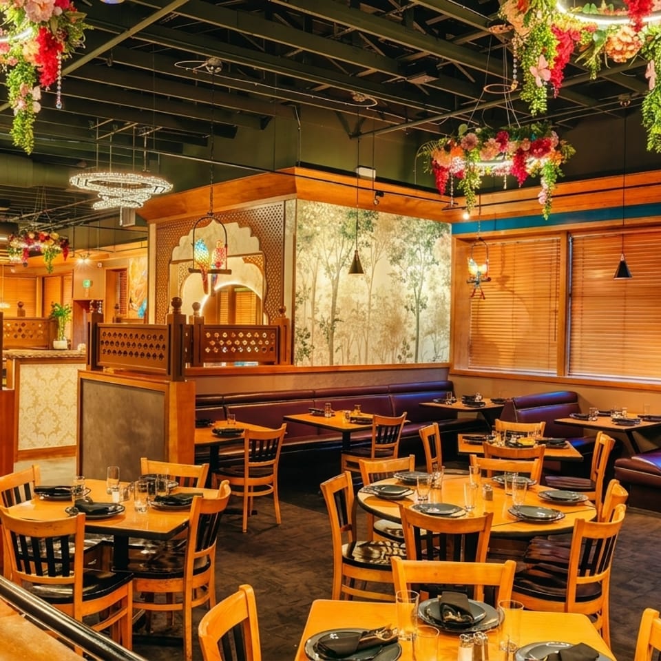 Warmly lit restaurant dining room with wood tables, leather booths, floral ceiling arrangements, chandeliers, and decorative lanterns.