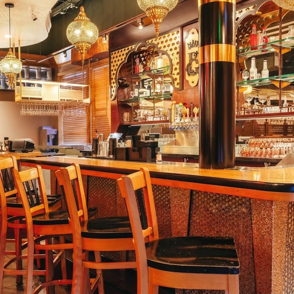 Elegant restaurant bar with ornate pendant lights, decorative tilework, mirrored liquor shelves, and rows of wooden barstools.