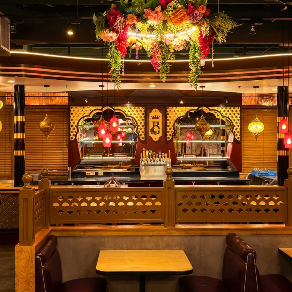 Warmly lit restaurant interior with wooden booths, buffet counters, pendant lights, and a colorful hanging floral arrangement.