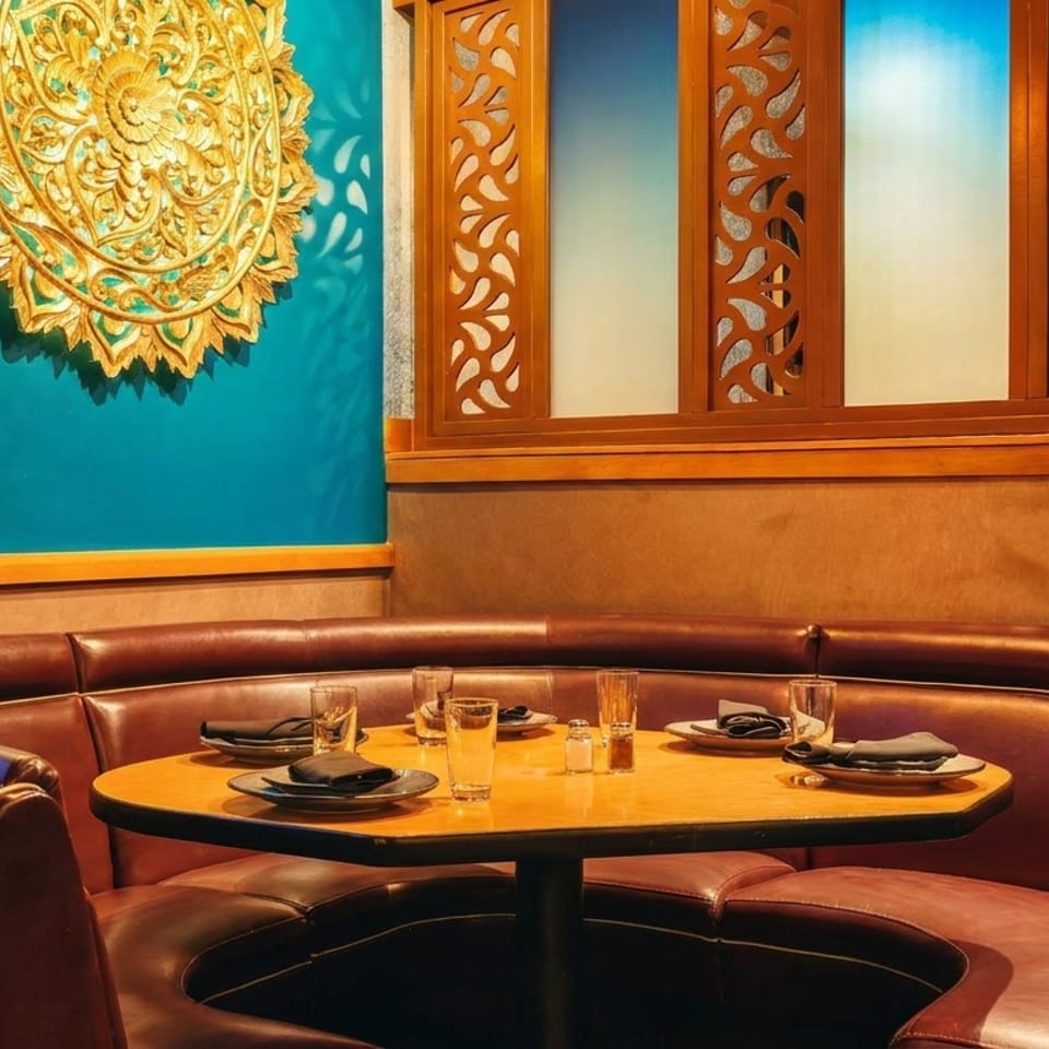 Elegant restaurant booth with a set table, leather seating, carved wooden screens, and ornate gold wall decoration.
