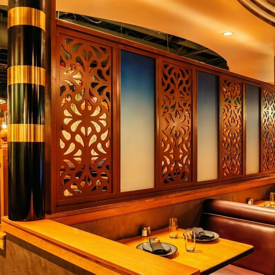 Warmly lit restaurant interior featuring wood-paneled booths, ornate carved room dividers, black-and-gold columns, and set dining tables.